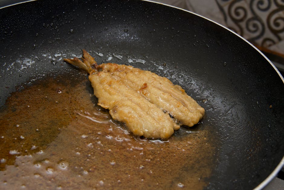 Close-up of a golden fried fish fillet cooking in a skillet with oil.