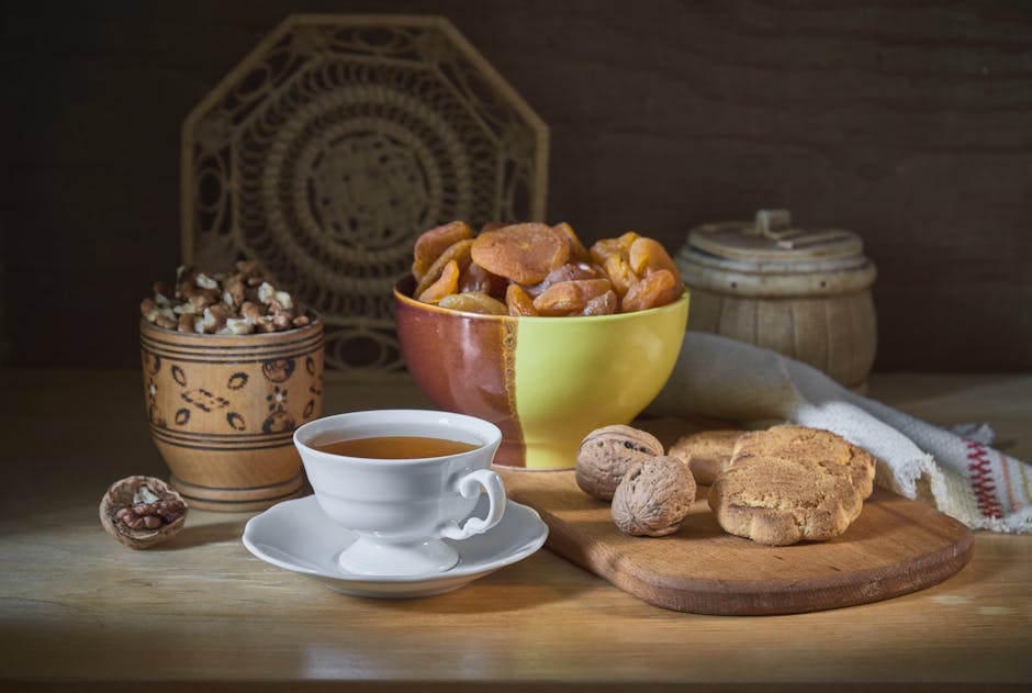 A rustic wooden table with tea, walnuts, dried apricots, and biscuits artfully arranged.